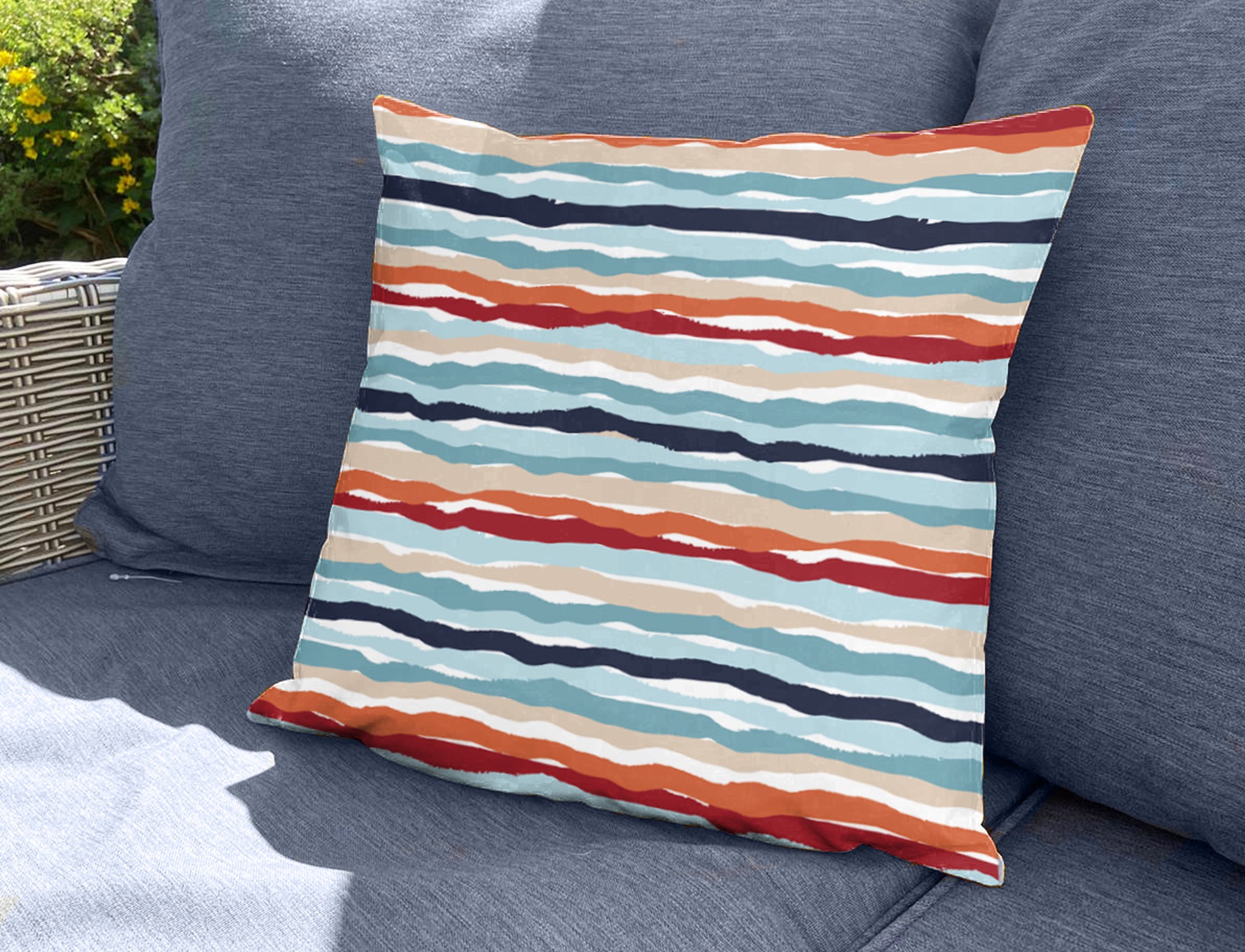 A square, coral and white striped throw pillow sits on a couch with a blue and white striped pattern.
