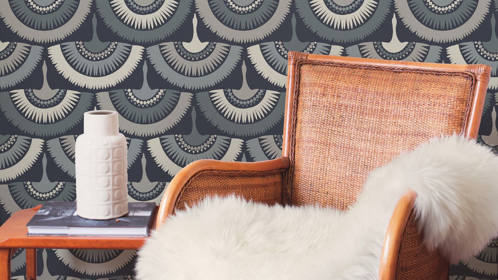 The wallpaper has a blue background with a white and grey feather pattern. The feathers are arranged in a staggered pattern, and they look like they are blowing in the wind. There is a brown armchair in the foreground, and a white vase and book on a side table in the background.