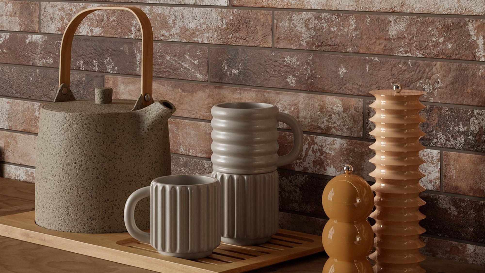 A kitchen countertop with a rustic brick wall backdrop. A wooden tray holds a teapot, a stack of mugs, and a set of salt and pepper shakers. The overall aesthetic is warm and inviting, with a focus on natural materials and earthy tones.