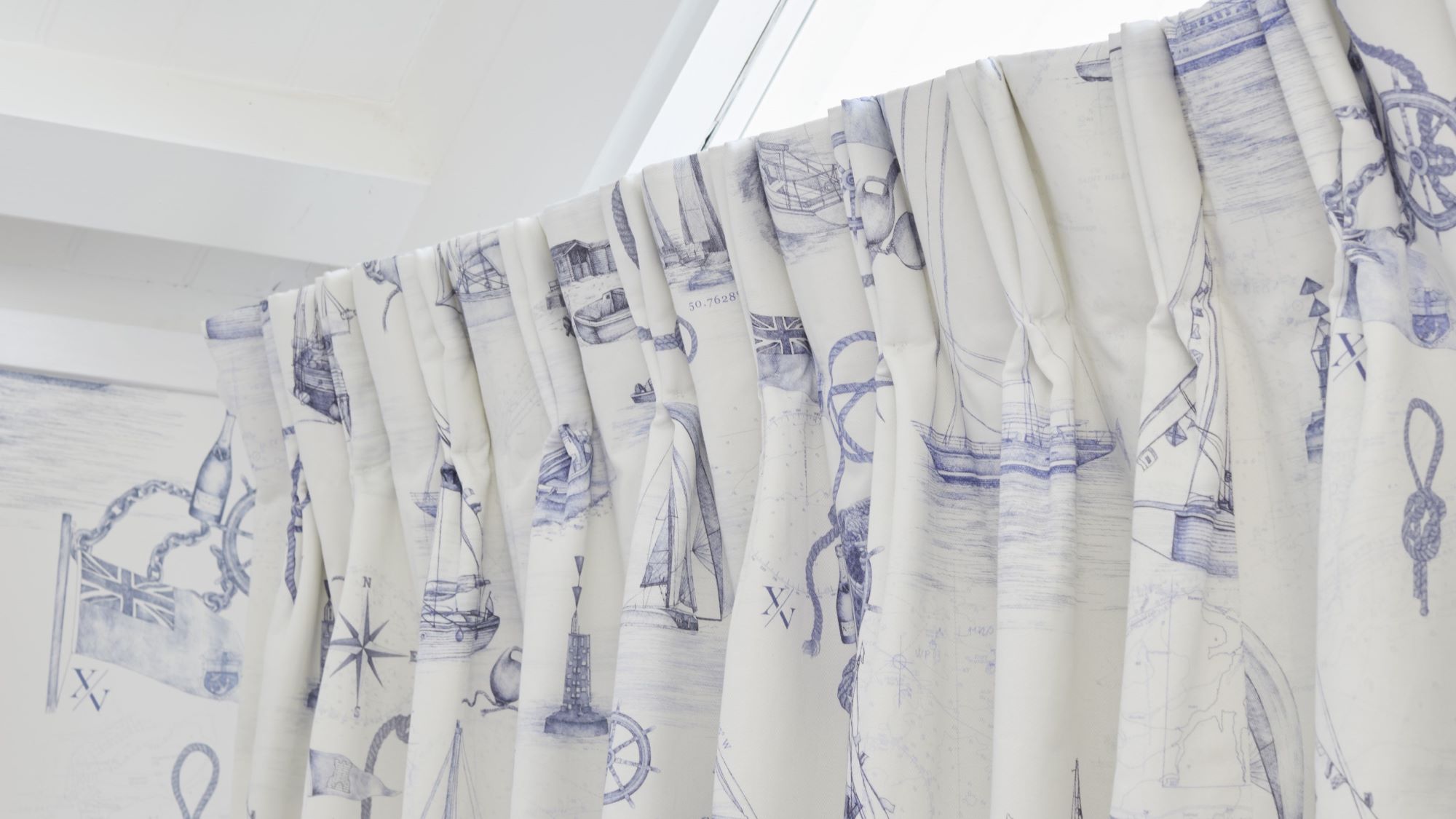 The curtains are white with a blue nautical pattern featuring boats, ships, and anchors. The rod is white and appears to be curved.